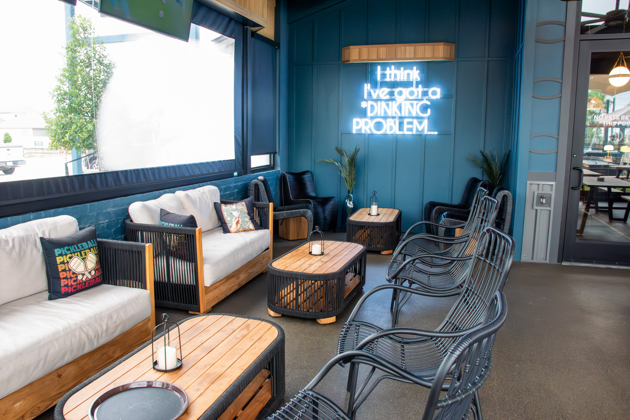 Covered patio lounge with sofas, lantern-lit coffee tables, and a neon sign