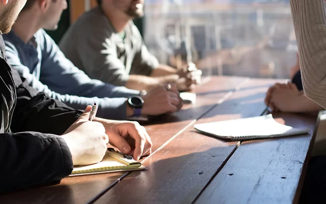 Team members seated at a table taking notes during a collaborative planning meeting