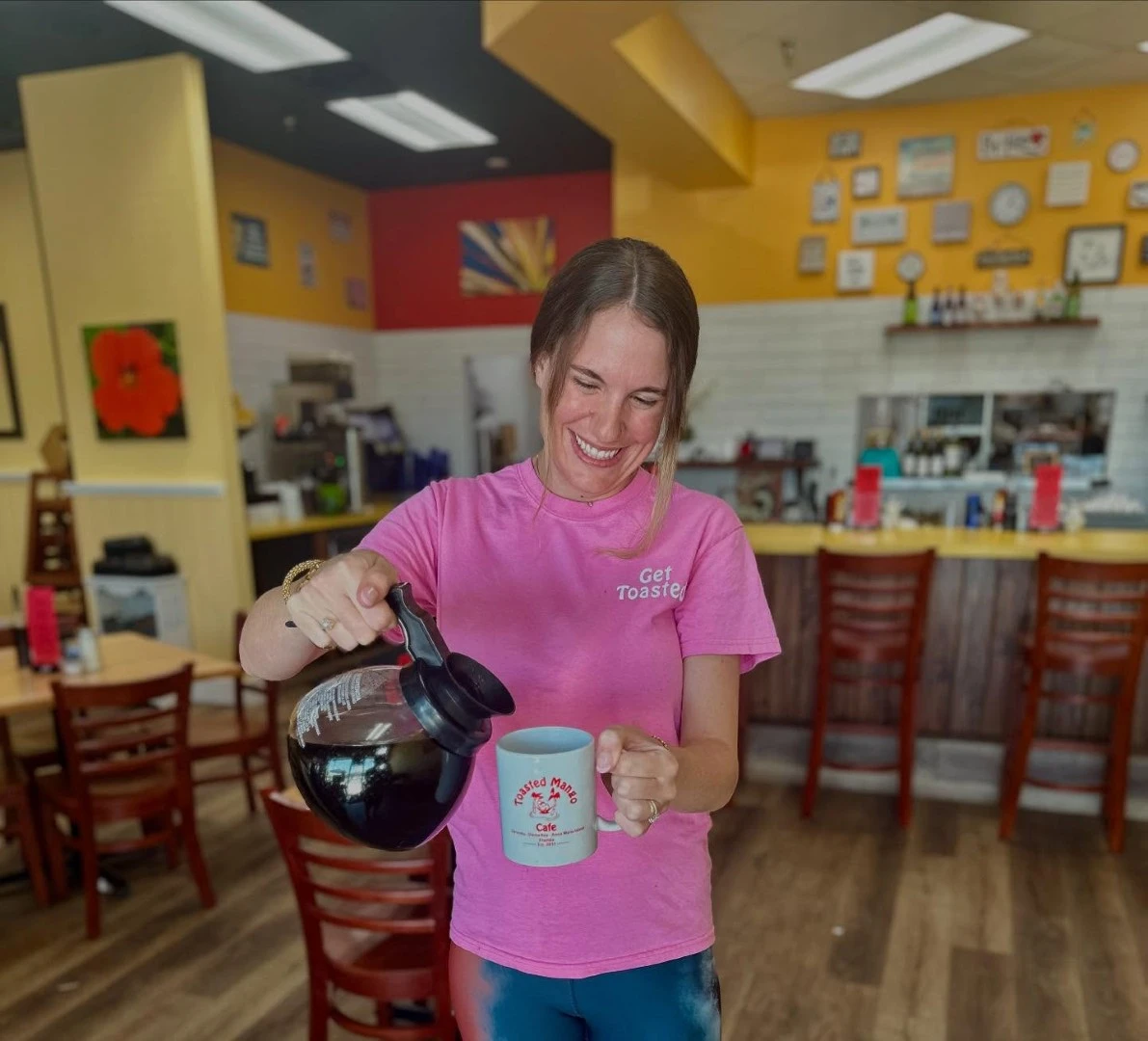 Staff member pouring fresh coffee into mug inside Toasted Mango Cafe dining area