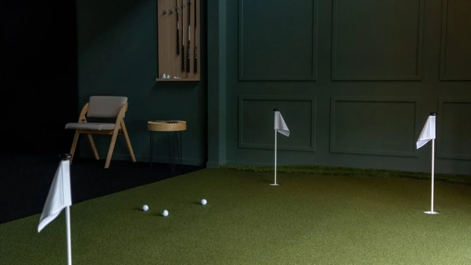 Indoor putting green practice area with golf balls, flag pins, and dark green paneled walls