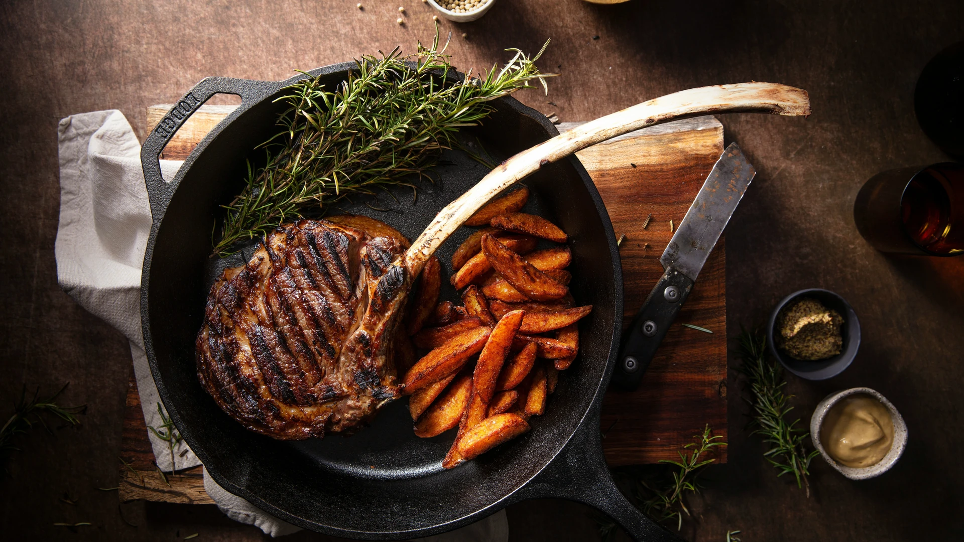 Grilled tomahawk steak with potato wedges and rosemary in a cast-iron skillet