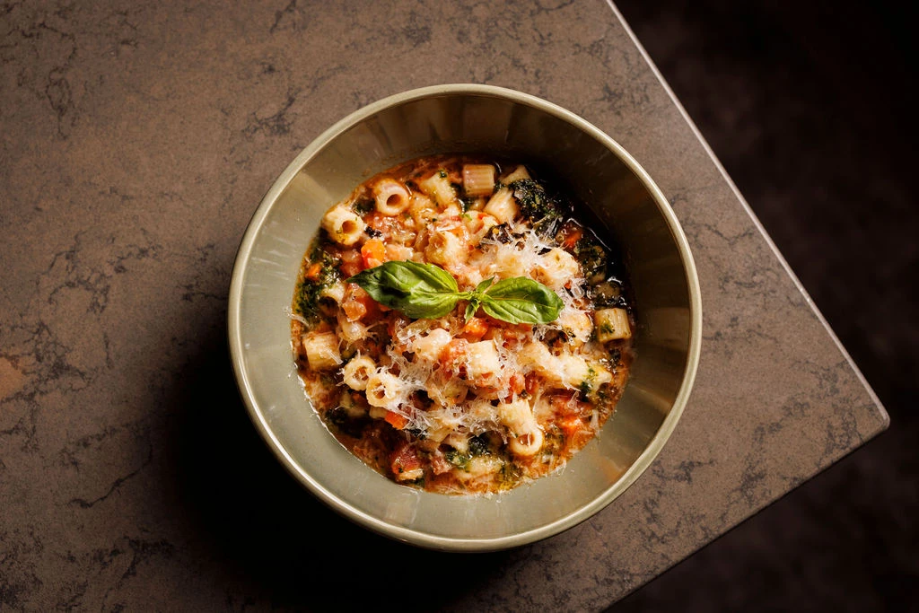 Bowl of pasta with tomato sauce, herbs, and grated cheese topped with fresh basil