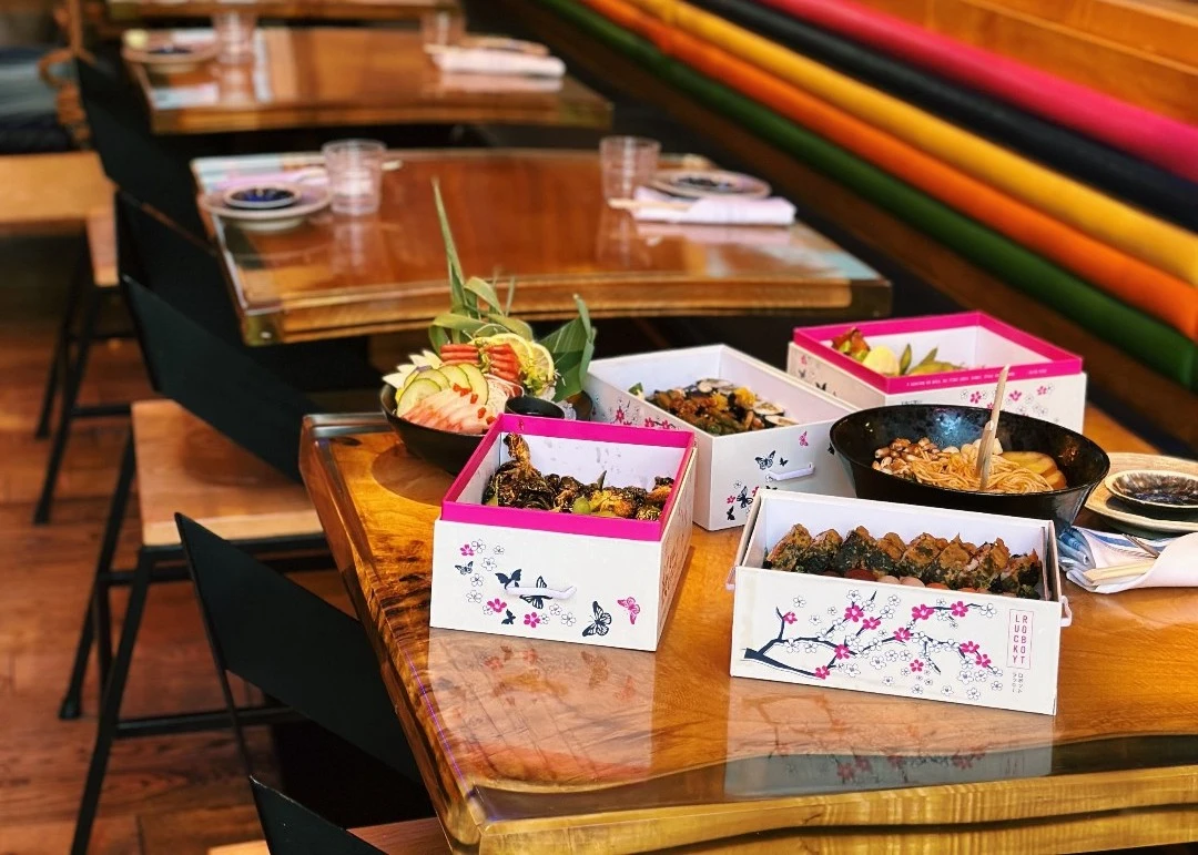 Japanese-inspired dining table featuring assorted dishes, sushi, noodles, and decorative serving boxes
