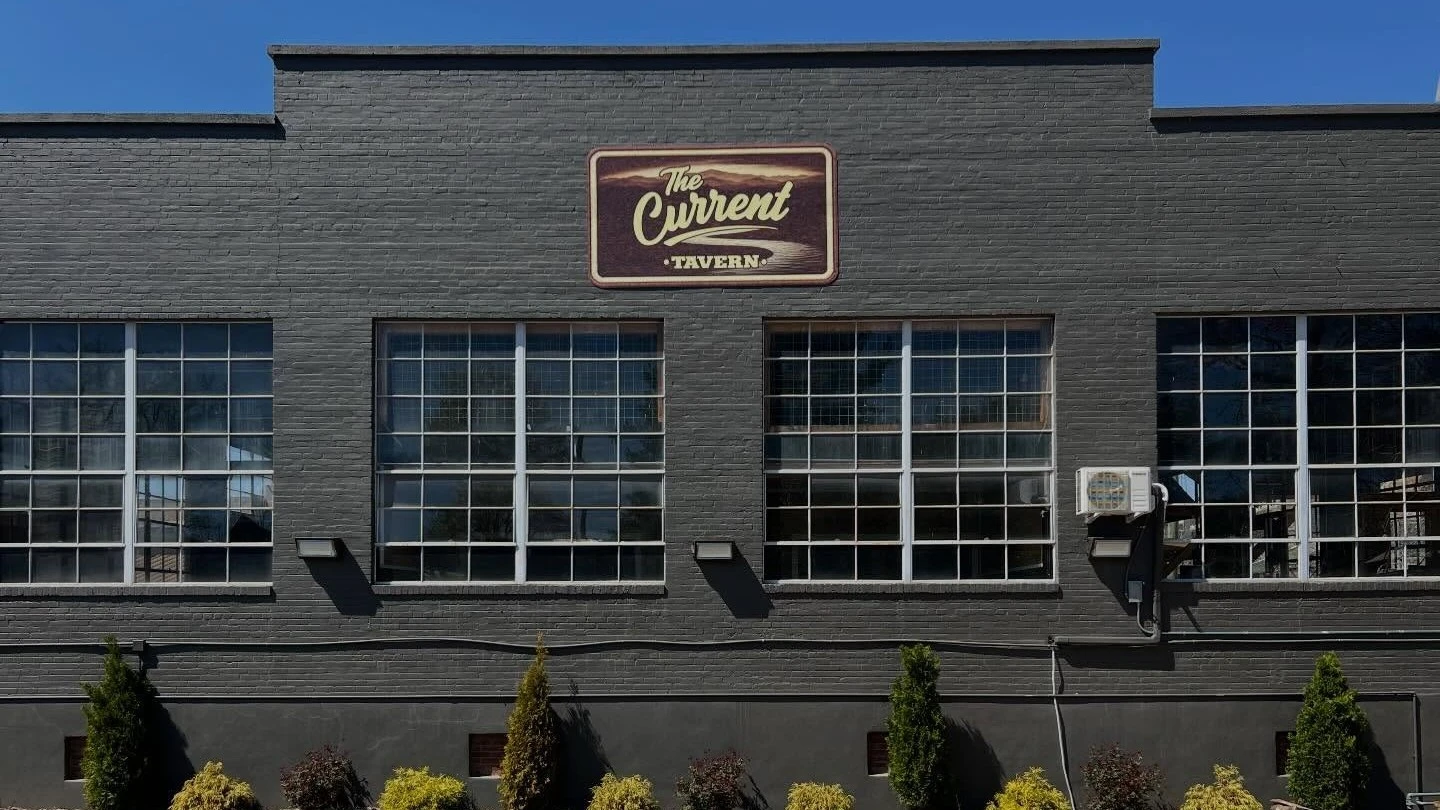 Exterior view of The Current Tavern building with large industrial-style windows and mounted restaurant sign
